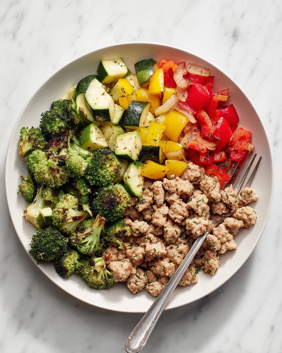 A white plate is filled with a mix of cooked vegetable and meat pieces. The dish has three layers: the bottom layer has small, light brown pieces of cooked meat seasoned with herbs, giving them a slightly speckled look; the middle layer shows bright green broccoli florets with charred edges, adding texture and color; the top layer is a mix of red and green bell pepper chunks, yellow zucchini slices, and pieces of translucent cooked onion, all scattered evenly on top. A silver fork rests on the right side of the plate, all set against a white marbled surface. photo taken with an iphone --ar 4:5 --v 7